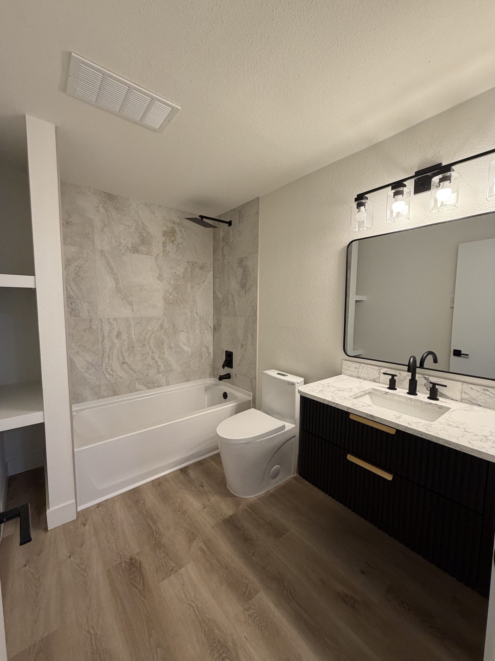 Alcove bathtub with marble-look surround, black fixtures and fluted black vanity