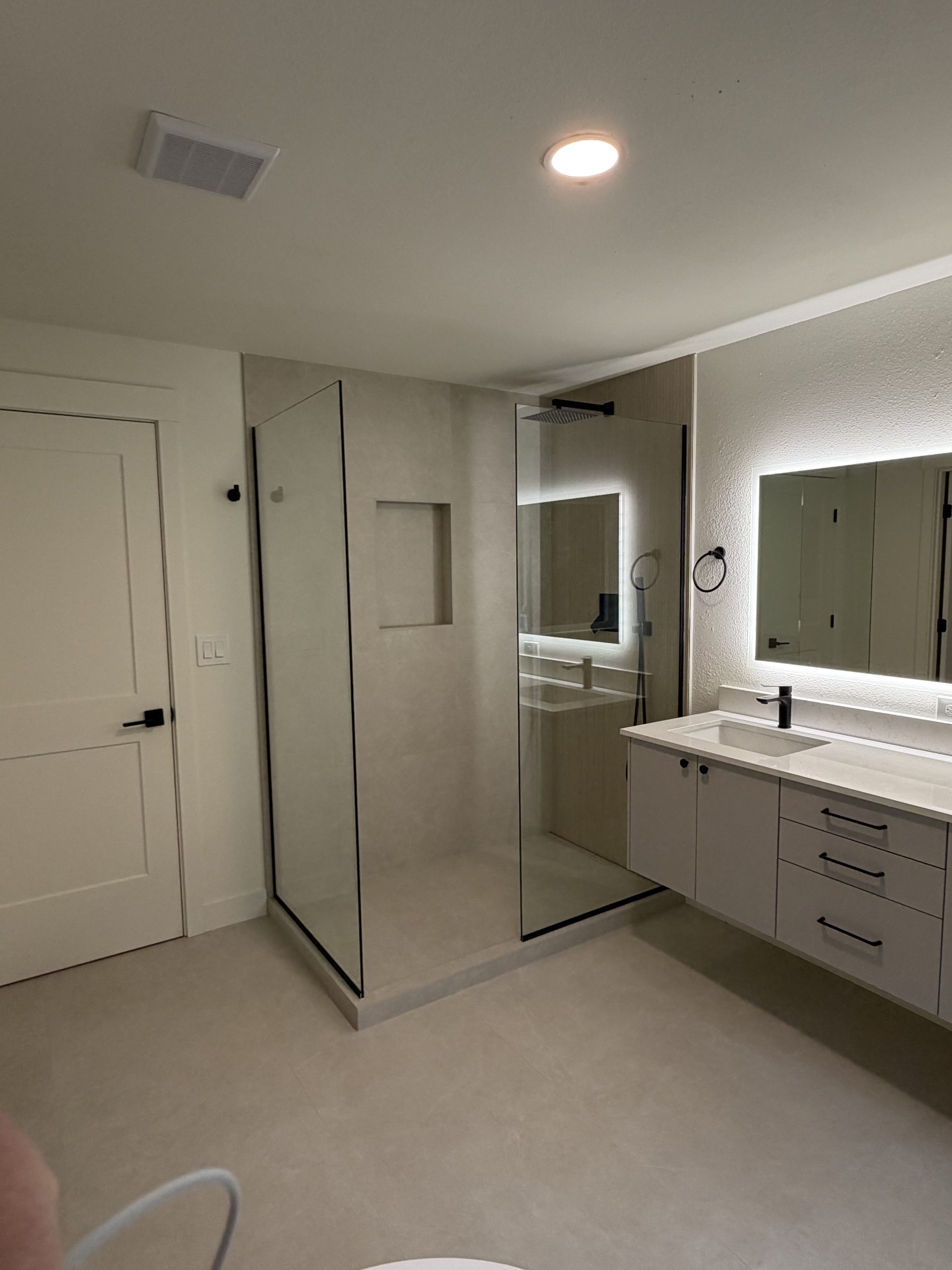 Moody walk-in shower with backlit mirror vanity