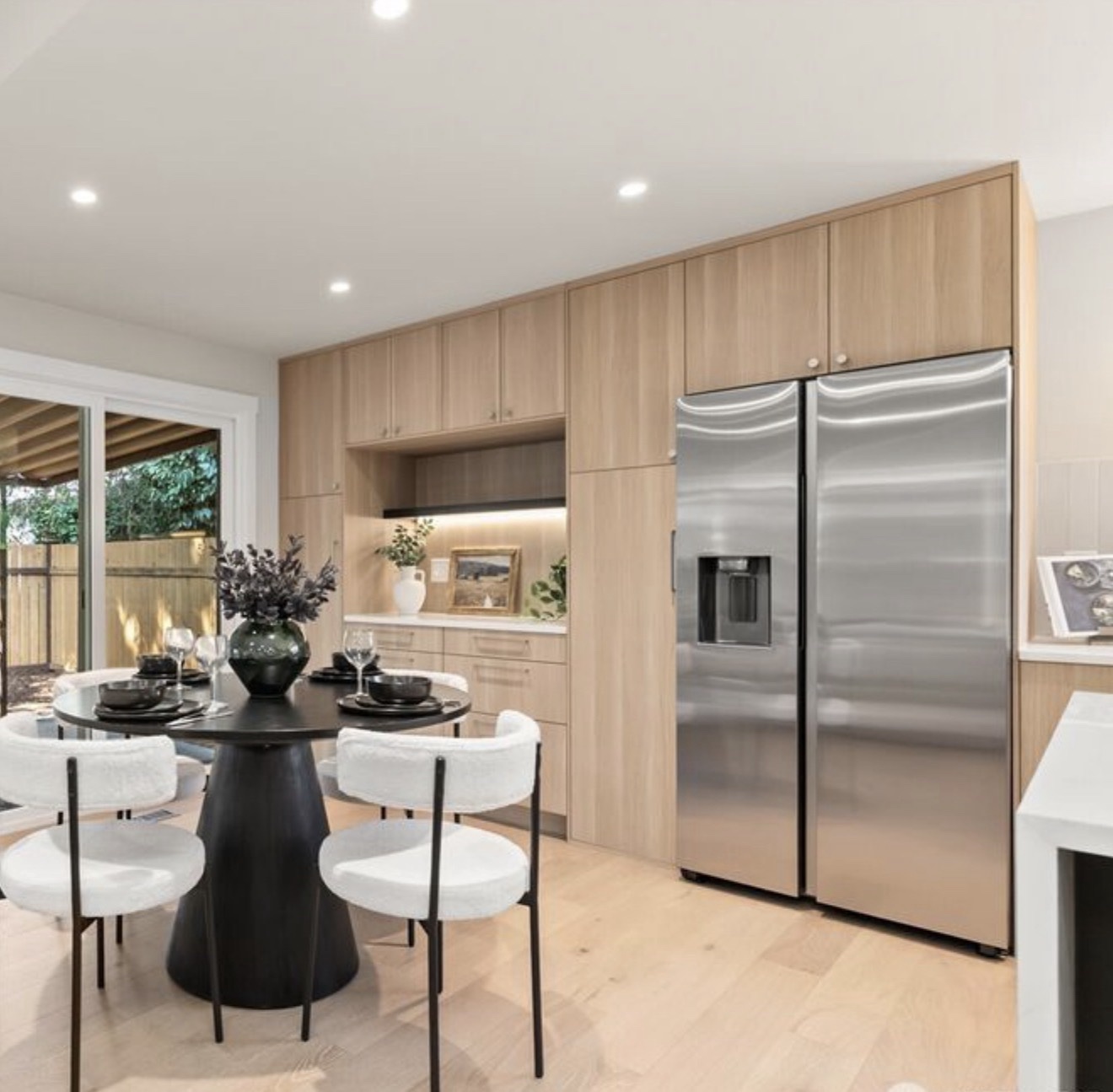 Kitchen and dining area with light wood cabinets, illuminated display niche and stainless side-by-side refrigerator