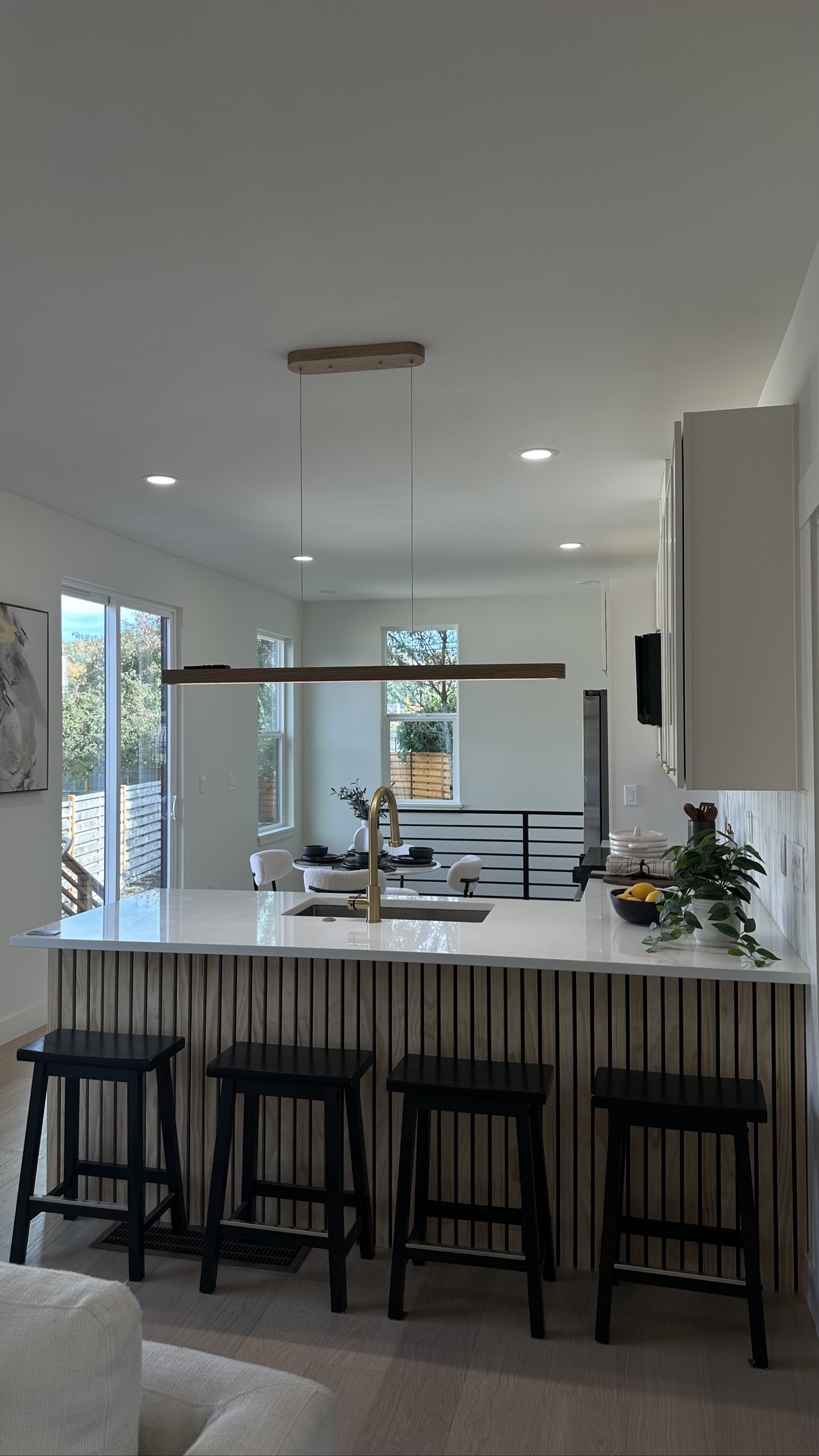 Kitchen island with fluted wood paneling, black bar stools and brass faucet