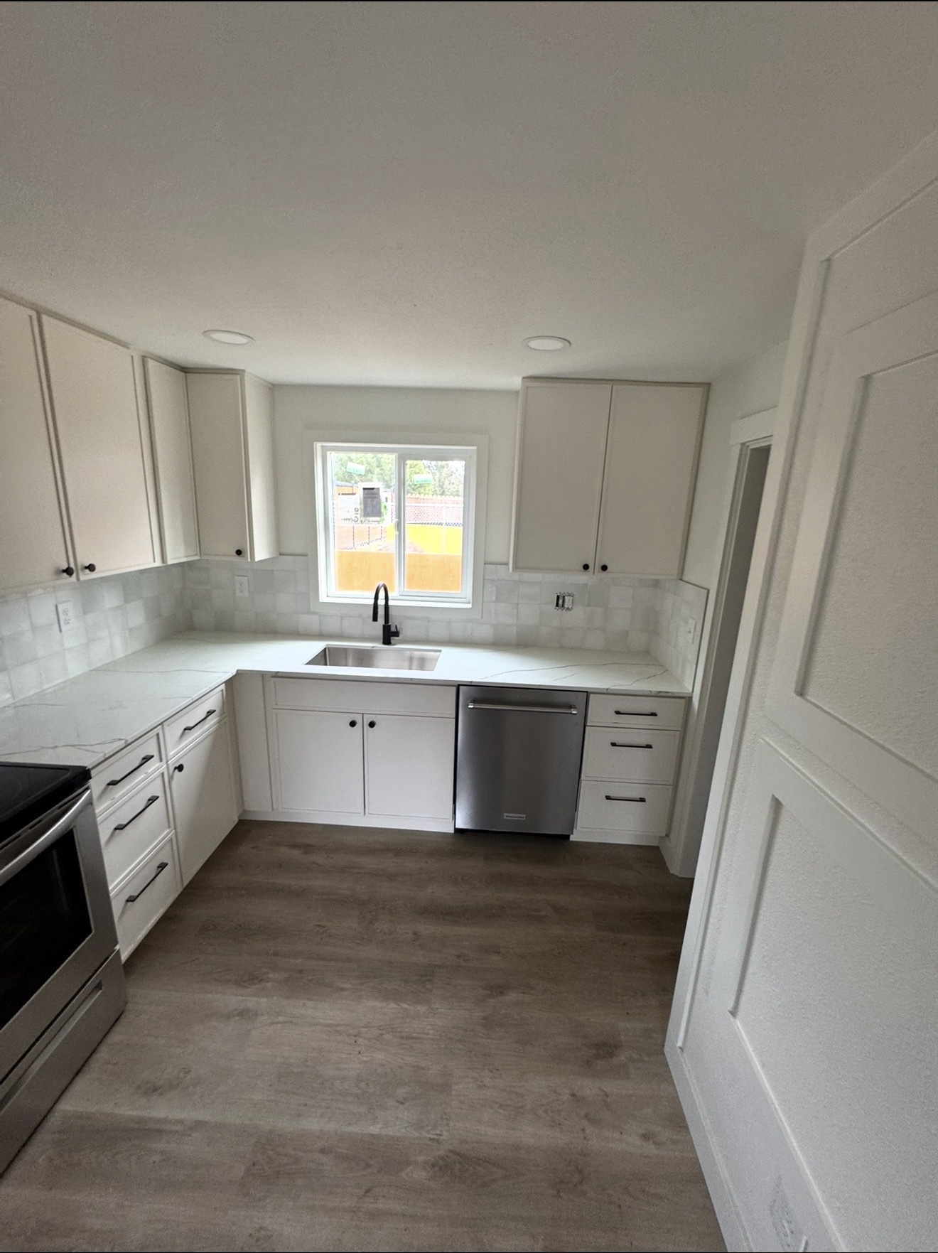 White shaker kitchen with marble-look counters, square tile backsplash and black faucet